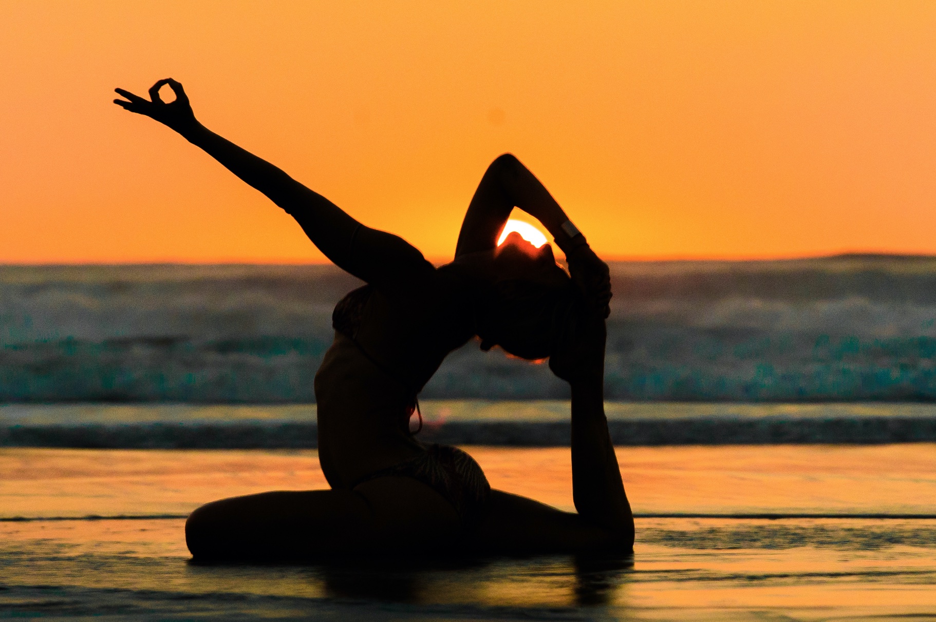 Shiva Rea in a sun-salutation silhouette at sunset over the ocean