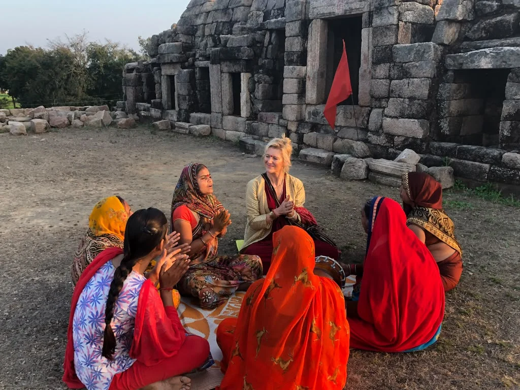 Shiva and a circle of women gathered beside a stone temple